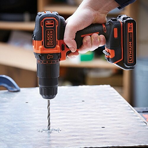 Hand holding Black & Decker drill on metal surface