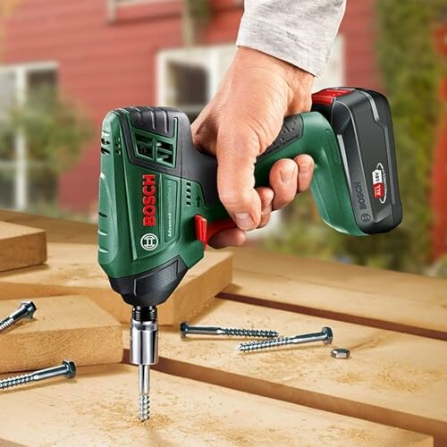 Person using a Bosch cordless drill on wood with screws nearby.