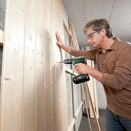 Man using a cordless drill on wooden boards.