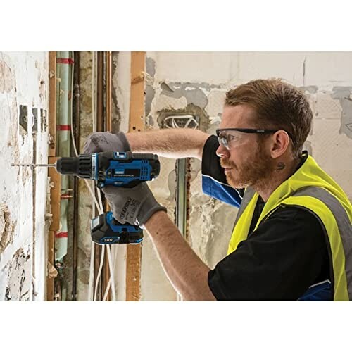 Man wearing safety gear using a drill on a wall.