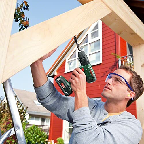 Man using a cordless drill on a wooden structure outdoors.