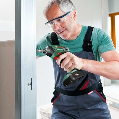 Man using a cordless drill on a metal frame.