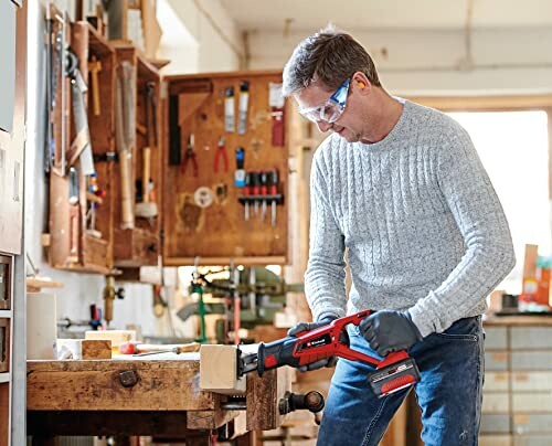 Man wearing safety glasses using a power saw in a workshop.