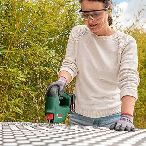 Person using a jigsaw tool on a patterned surface outdoors.