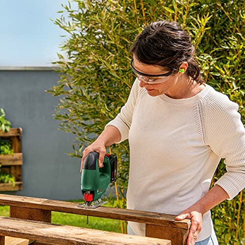 Woman cutting wood with a jigsaw outdoors