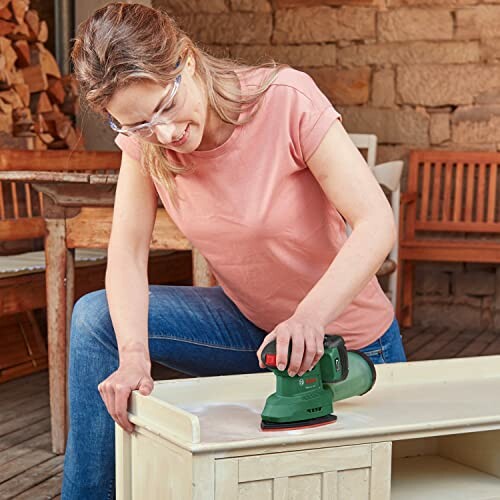 Woman using a green orbital sander on furniture indoors.